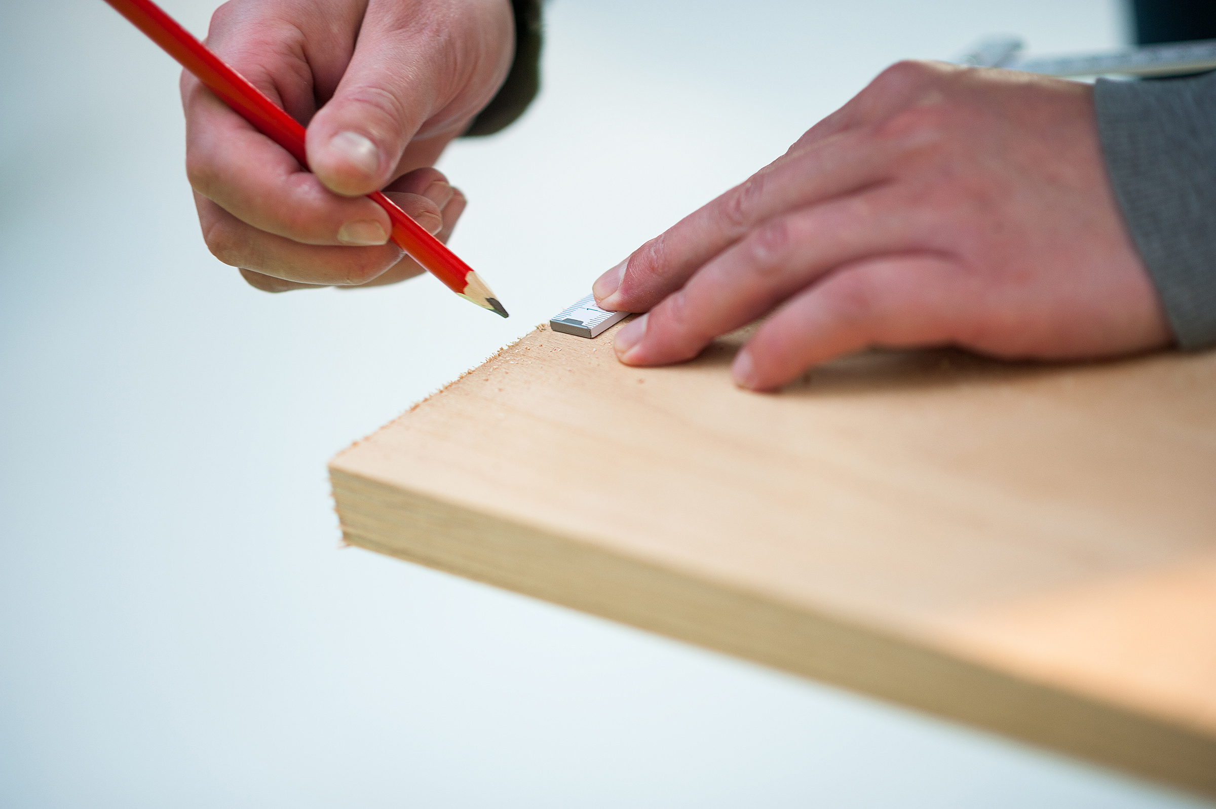 Ein Foto von den Händen eines Mannes, der mit einem Bleistift und einer Messlineal eine Holzplatte bemisst