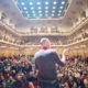 Ein Fotograf steht auf der Bühne vor dem Publikum in der Laeiszhalle im Rahmen einer Veranstaltung in Hamburg und trägt vor, fotografiert von einem Eventfotografen