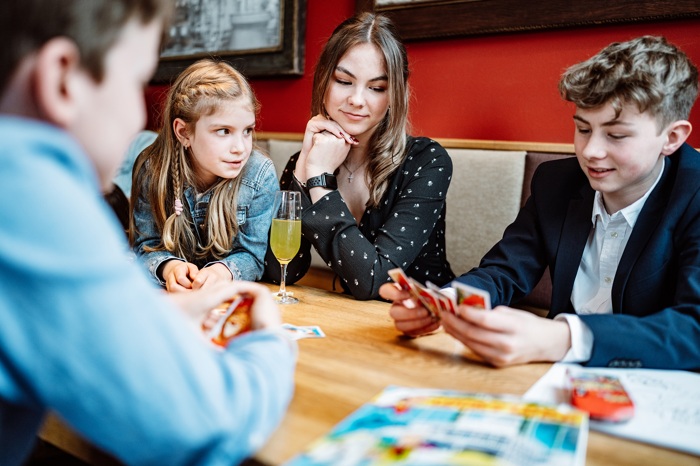 This documentary family photograph captures a group of young people intently playing a card game at a table, illustrating an authentic moment of family connection and fun.