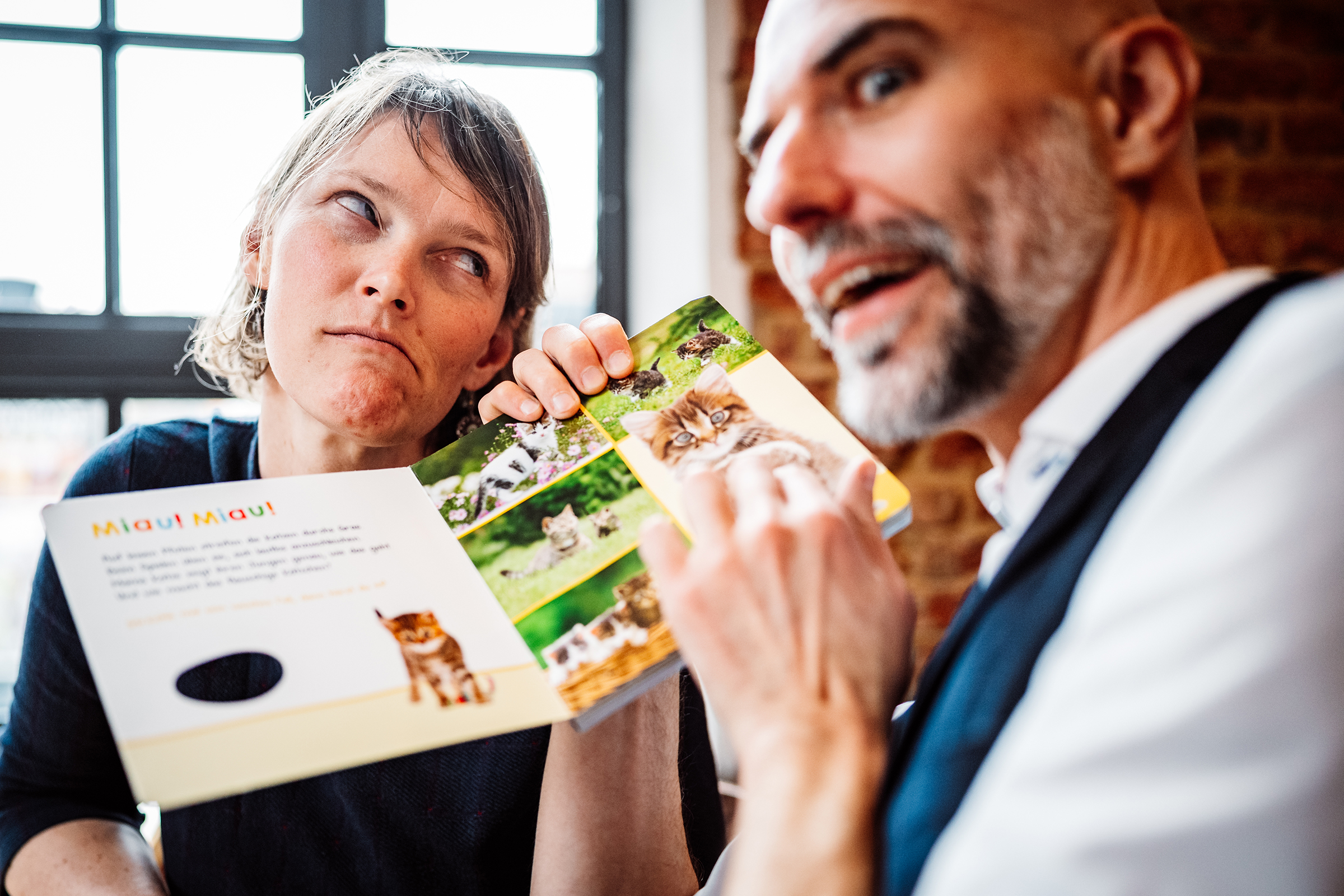 This humorous documentary family photograph captures a woman's playfully exasperated reaction as a man enthusiastically shows her a children's kitten book, showcasing an authentic and relatable family moment.