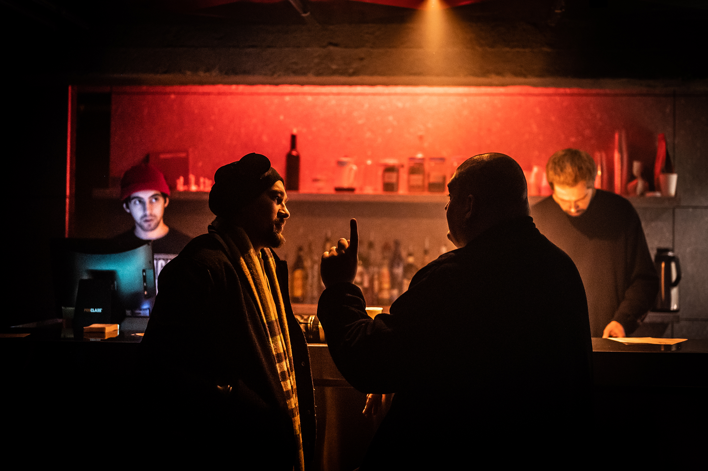 This atmospheric documentary photograph captures two men in an intense, authentic conversation at a dimly lit bar, highlighting the storytelling power of candid photography services.