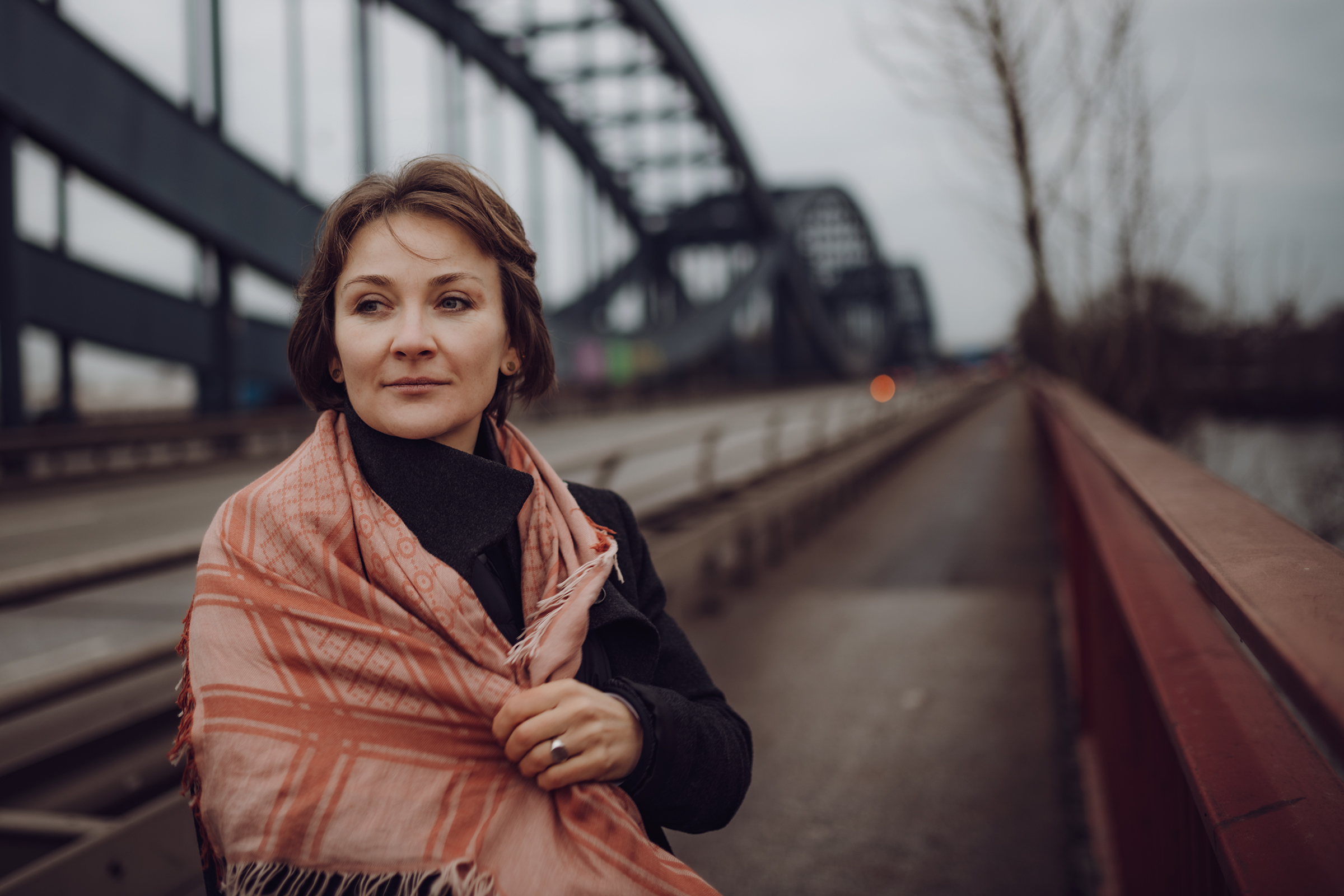 This atmospheric documentary portrait shows a woman wrapped in a patterned scarf on a bridge, her contemplative gaze exemplifying the authentic storytelling of family photography.