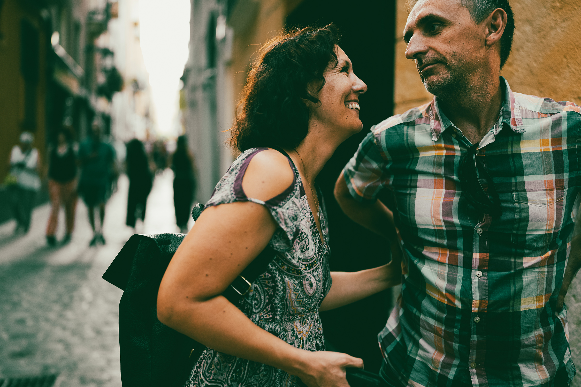 A candid documentary photograph captures a couple sharing a joyful, authentic moment on a bustling street, showcasing the storytelling power of family and relationship photography.