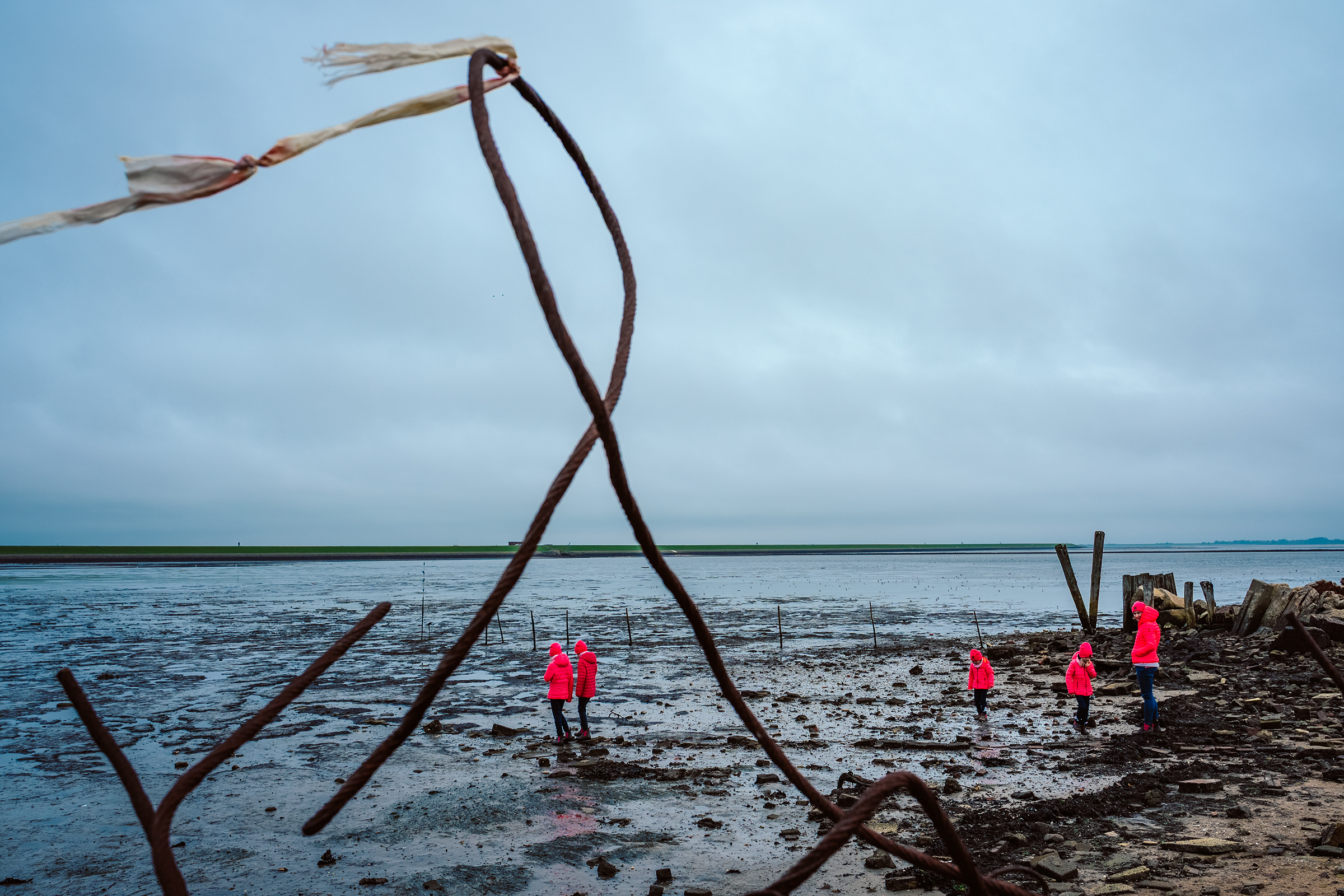 This documentary family photograph captures a group in vibrant pink jackets exploring a moody, expansive tidal flat, highlighting an authentic shared experience.