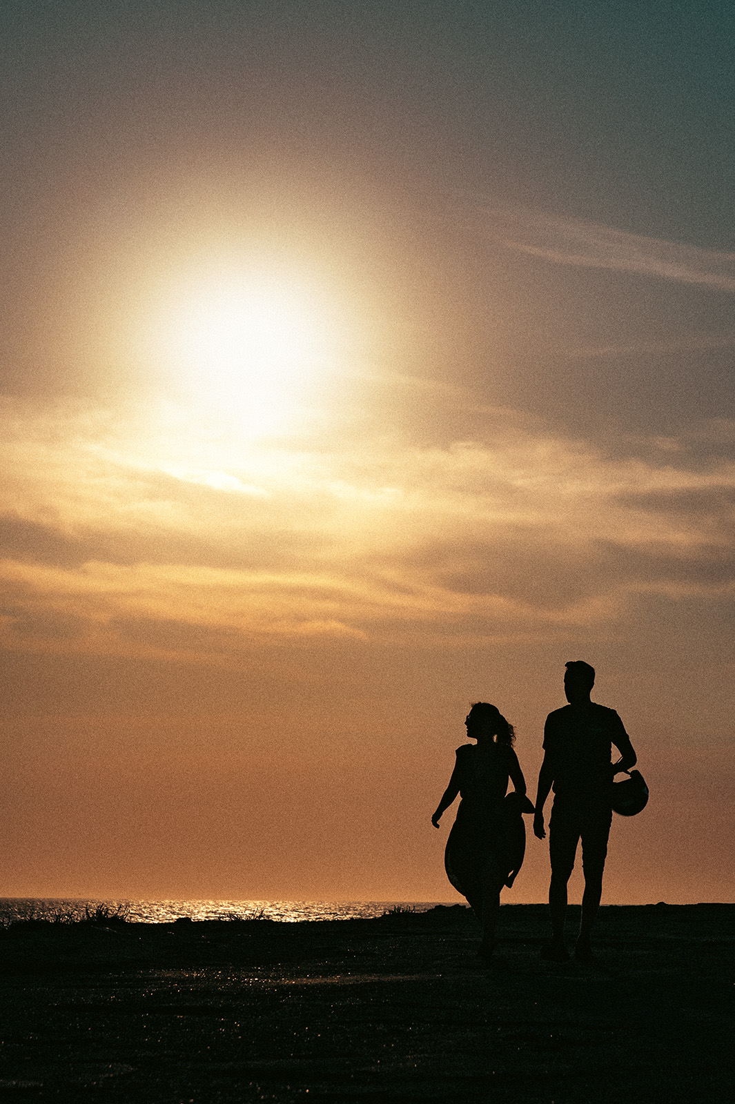 Silhouetted against a glowing sunset, a couple holding hands embodies a tender family story captured through authentic documentary family photography.