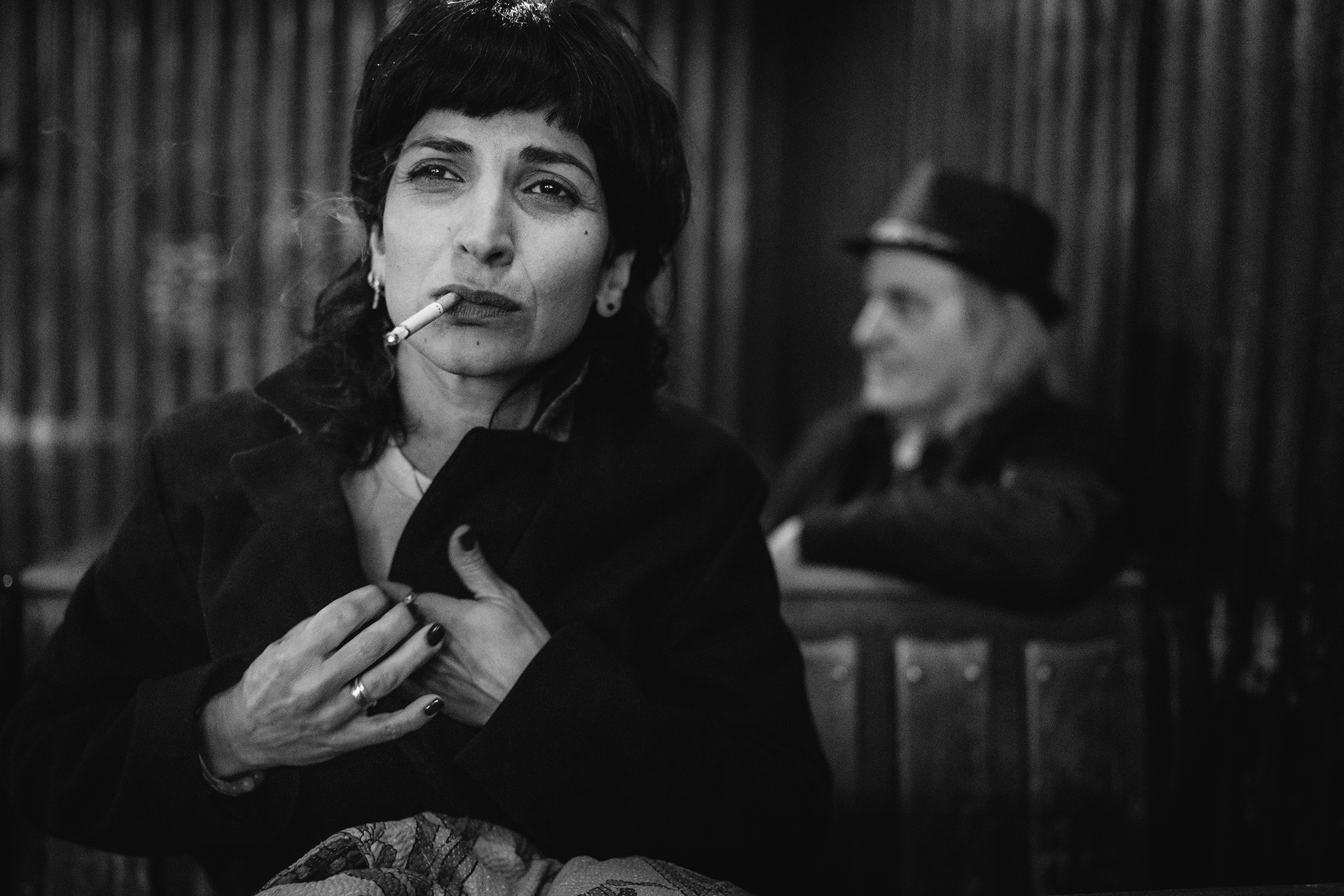 Candid black-and-white documentary photograph of a woman smoking and gazing pensively into the distance, capturing raw emotion and everyday intimacy in a shared moment.