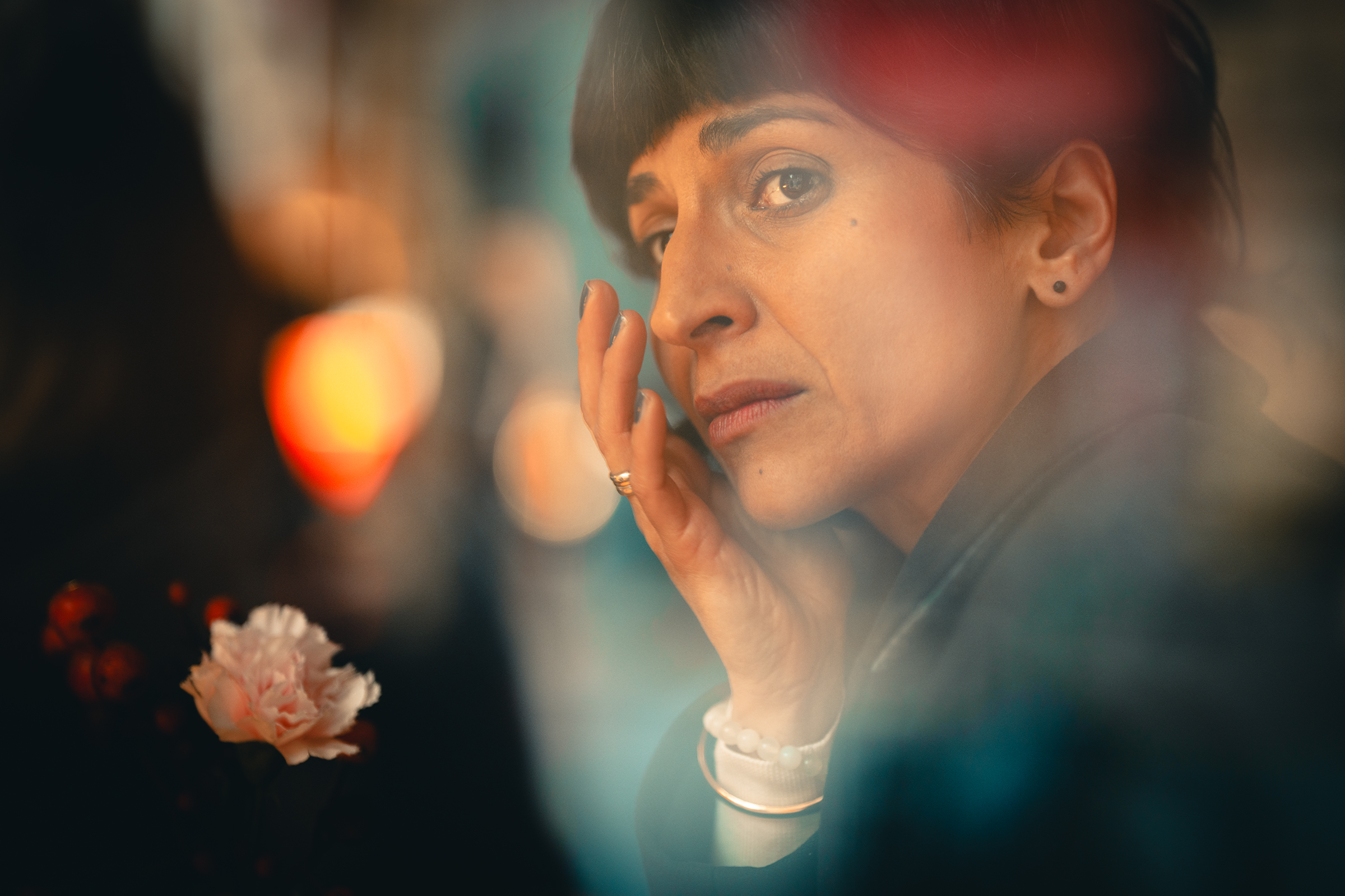 Documentary-style color portrait of a woman gazing thoughtfully through a window, her hand gently resting on her face, evoking quiet emotion and personal reflection.